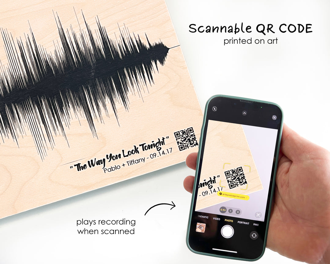 a hand holding a smartphone displaying a QR code printed on a piece of art, which appears to be a sound wave. The QR code is printed on the art and is being scanned by the smartphone.