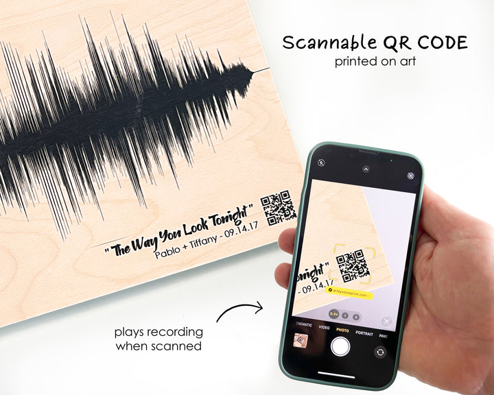 a hand holding a smartphone displaying a QR code printed on a piece of art, which appears to be a sound wave. The QR code is printed on the art and is being scanned by the smartphone.